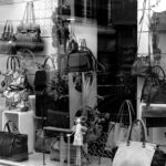 Black and white photo of a boutique window showcasing luxury handbags on display.